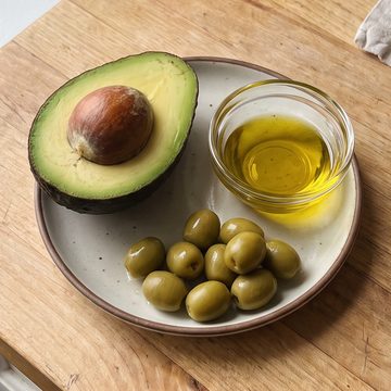 Half an avocado, green olives and a dish of olive oil