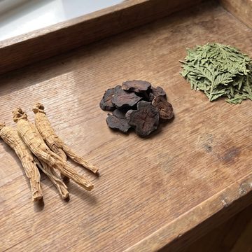 Dried ginseng roots, He Shou Wu slices and Biota leaves on a wooden tray